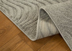 Beige quilted area rug with geometric pattern on wooden floor, corner detail