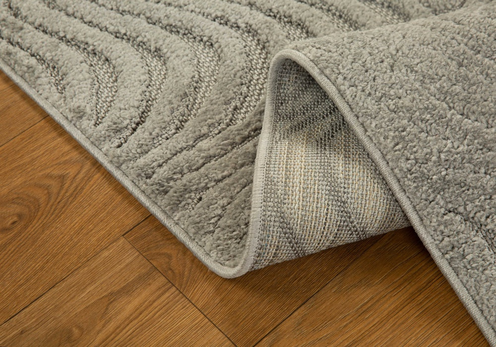 Beige quilted area rug with geometric pattern on wooden floor, corner detail