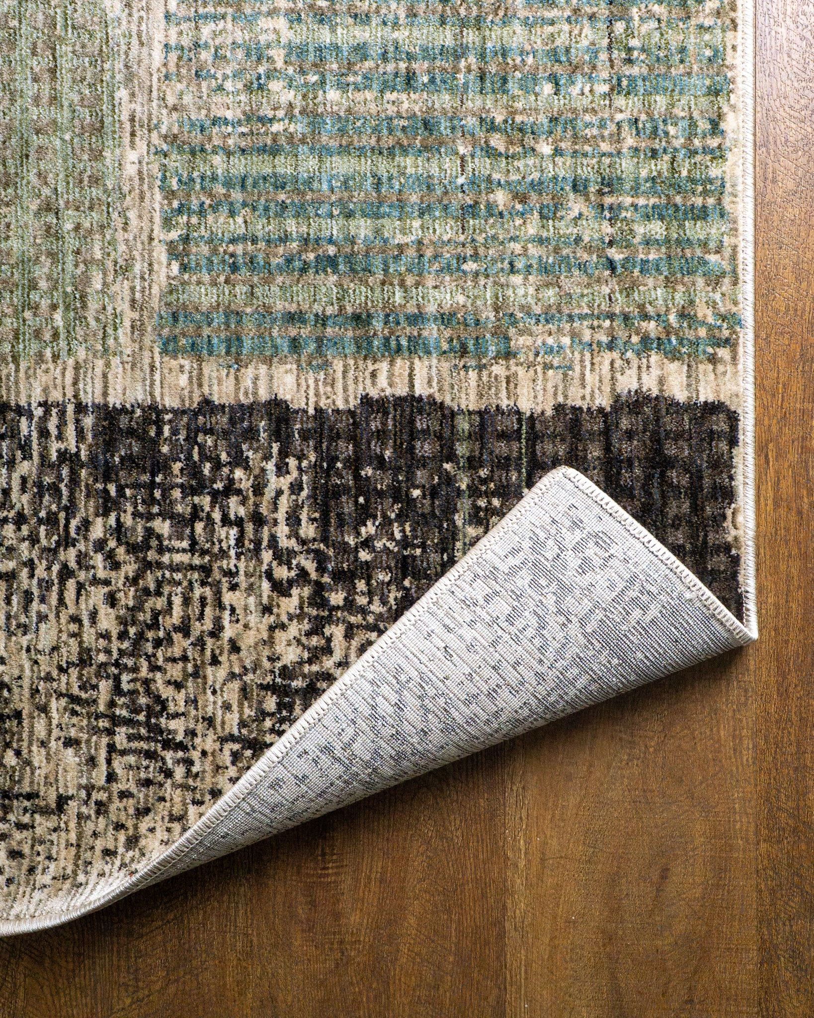Modern geometric patchwork rug in green, black, and neutral tones with textured weave