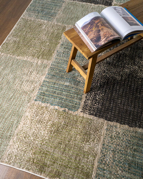 Modern geometric patchwork rug in green, black, and neutral tones with textured weave