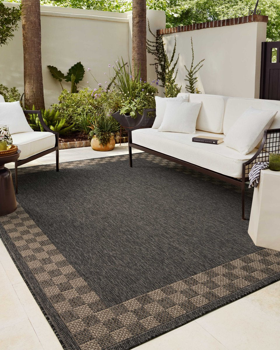 Charcoal grey and tan bordered outdoor rug in modern patio seating area