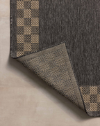 Charcoal grey and tan bordered outdoor rug in modern patio seating area