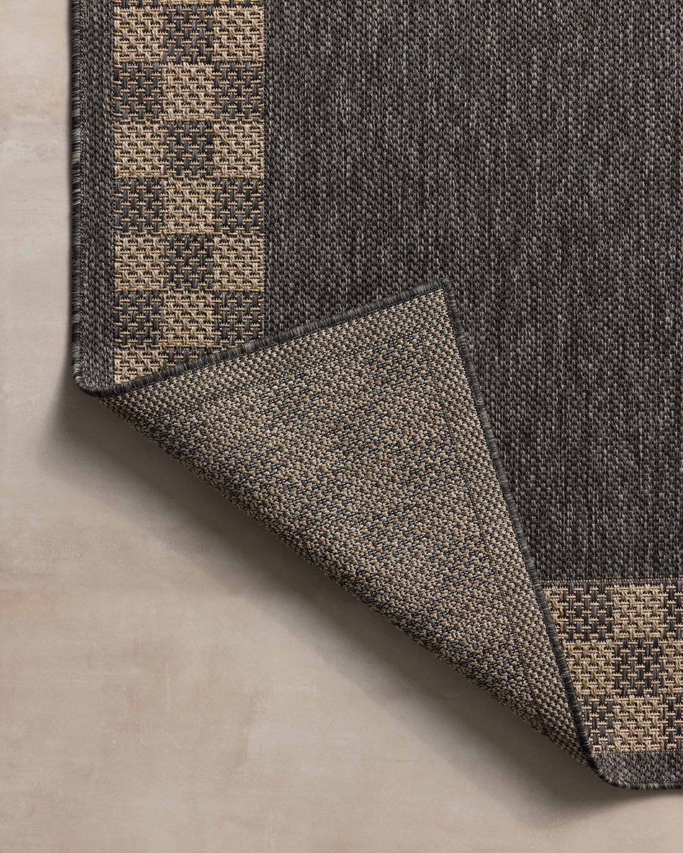 Charcoal grey and tan bordered outdoor rug in modern patio seating area