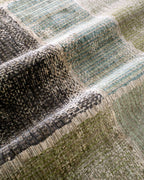 Modern geometric patchwork rug in green, black, and neutral tones with textured weave